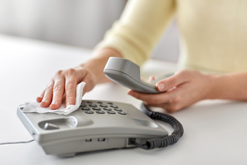 hygiene and disinfection concept - close up of woman hands cleaning desk phone with paper tissue