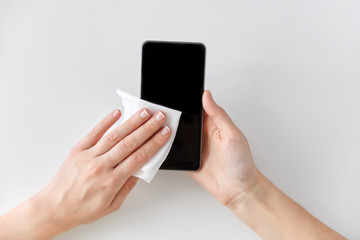 hygiene and disinfection concept - close up of woman hands cleaning smartphone with tissue