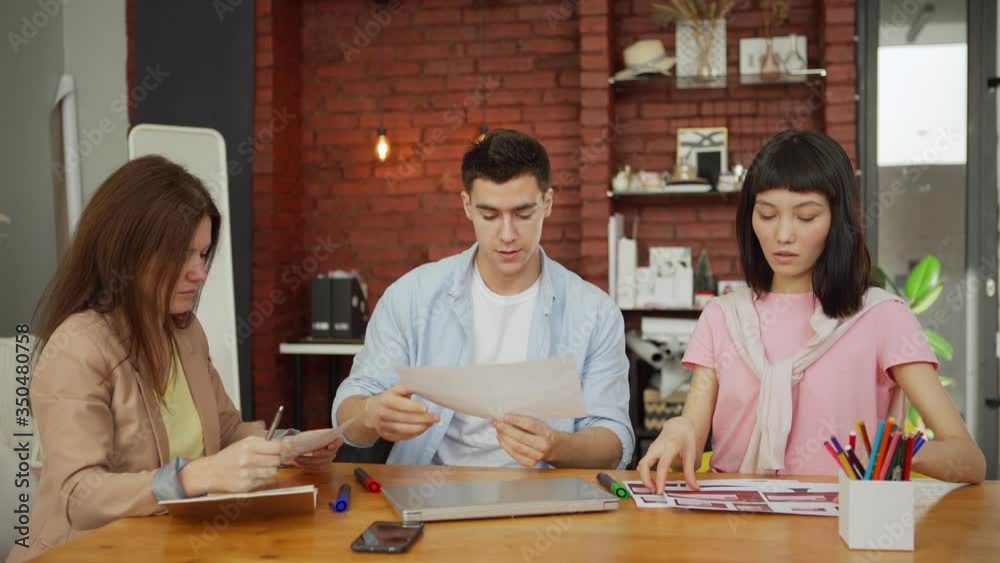 Wall mural creative startup business team of three discussing printouts with website interface templates while 