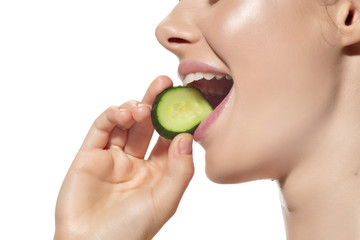 Close up of beautiful young woman with cucumber's slice over white background. Concept of cosmetics, makeup, natural and eco treatment, skin care. Shiny and healthy skin, fashion, healthcare.