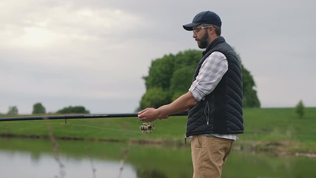 A young bearded man fishing on a lake, a fisherman holding a fishing rod in his hands