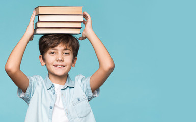 Young boy holding stack of books on head