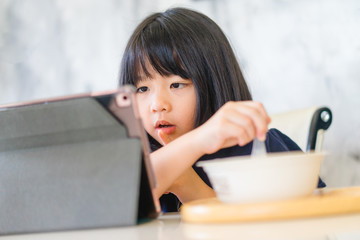 Asian girl student online learning in class study.Online video call with teacher.Child girl eating rice congee breakfast with laptop at home.New normal.Covid-19 coronavirus.Social distancing.stay home