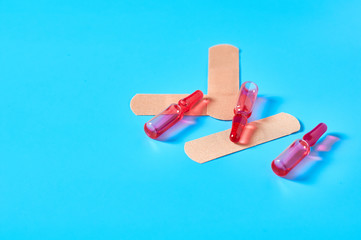 Heap of sticky medical patch near red vaccine on blue background. Healthcare concept