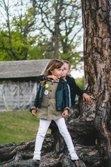 Naklejka premium Two pretty cute children boy and girl standing near big tree trunk in summer park outdoors.