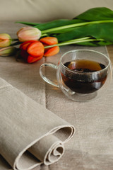 a clear glass cup with hot black tea, a bouquet of red tulips are on the table. spring tea party