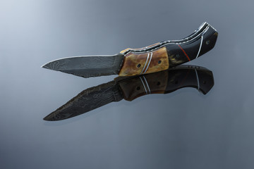 folding pocket knife on a mirrored surface, blade made of multi-layer Damascus steel, handle made of Damascus steel, bone pads, aluminum spacers