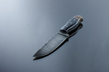 an all-metal, middle kitchen knife lies on a mirror surface, a blade made of multilayer damask steel, lining from deer antler and walnut burl