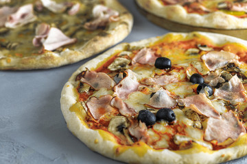 baked pizza with olives, mushrooms, ham, topped with melted cheese, on a wooden table, on a background of baking