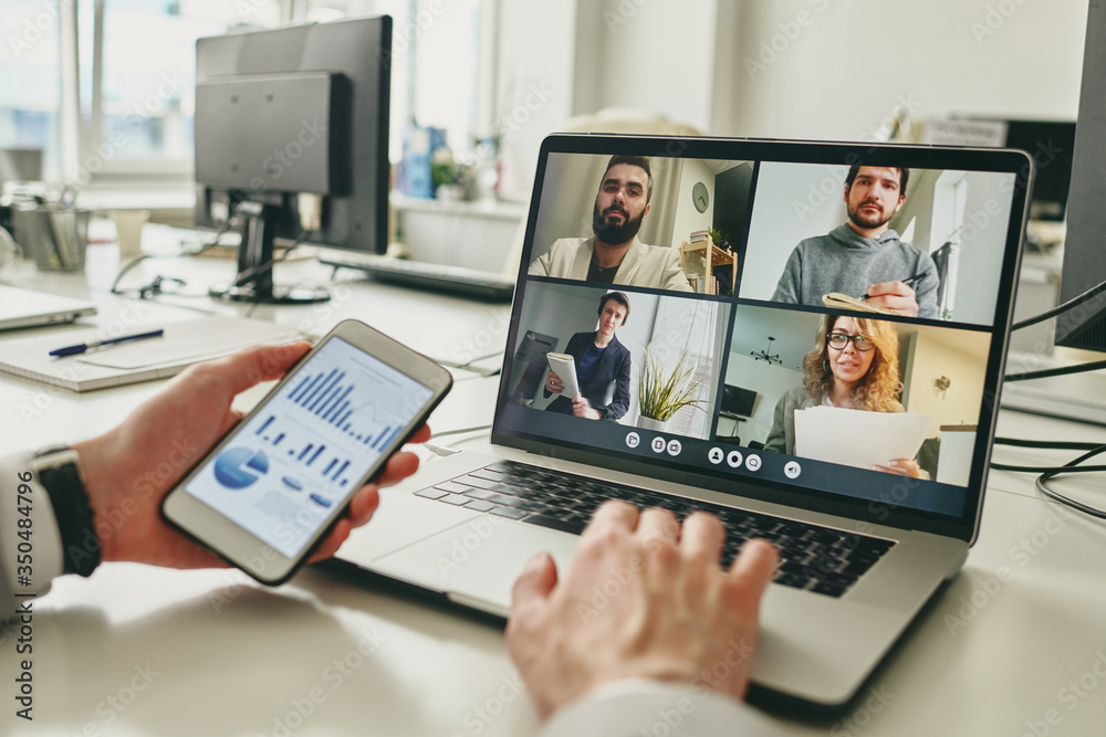 Poster Close-up of businessman working in empty office and using smartphone to view graph while discussing sales with colleagues via video conferencing app