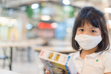 Asian kid girl in canteen at school.Student girl wearing fabric face mask sitting distancing in restaurant in shopping mall.Social distancing concept.Partition board for separated in restaurant.People