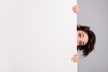 Closeup photo of funny pretty lady holding hands empty paper poster proposing advert place look interested peeking eyes tricky crazy person isolated grey color background