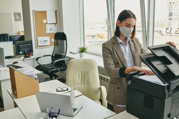 Young office woman in cloth mask scanning document in empty office during coronavirus epidemic