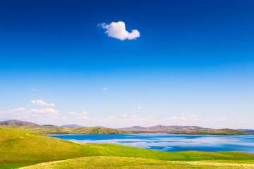 Obraz na płótnie Canvas Beautiful lake with green hills and the blue sky with white clouds. Spring nature landscape. South Ural, Bashkortostan Republic, Russia.