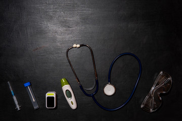 Stethoscope, thermometer, oxymeter, syringe and test tube on a black background. Doctor’s equipment for taking tests for infection with the virus Covid-19