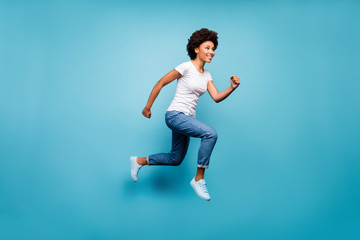 Fototapeta na wymiar Full length photo of funky dark skin curly lady jumping high sporty person rushing discount shopping final day wear casual white t-shirt jeans isolated blue color background