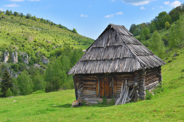 Fototapeta na wymiar Lonely old wood house on a mountain hill with green grass against blue sky