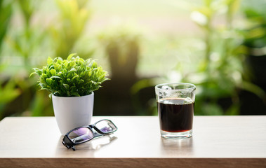 Obraz na płótnie Canvas Hot coffee and a small plant pot with glasses placed on a piece of wood with a blurred tree background.