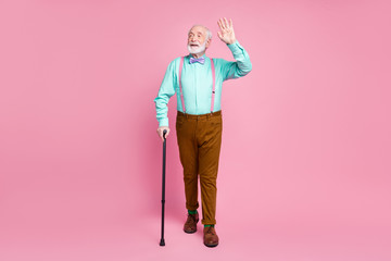 Fototapeta premium Full size photo of cool grandpa move street with help of walking stick waving arm see friends wear shirt suspenders bow tie trousers shoes socks isolated pink pastel background