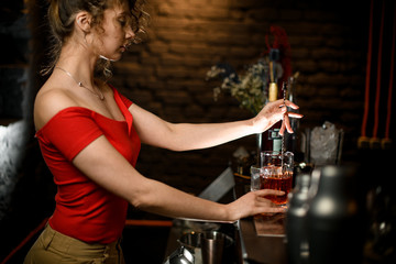 lady at bar gently stirring drink in cup with bar spoon