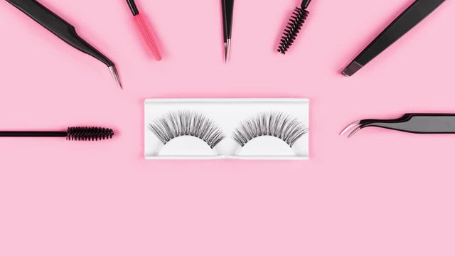 Fake eyelashes. Tools for eye lash extensions on trendy pastel pink background. Concept. Eyelash curler, tweezers, brushes. Makeup accessories. Cosmetic products. Top view. Stop motion. Beauty pattern