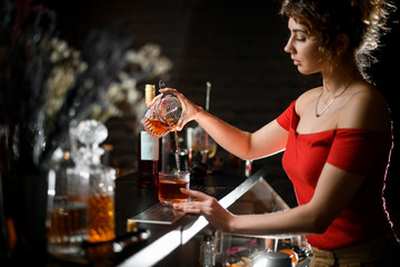 Pretty woman in red blouse pours cocktail from mix bowl into glass