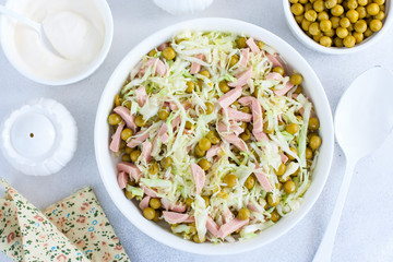 vegetable salad with cabbage, sausages and canned peas on a white plate, selective focus