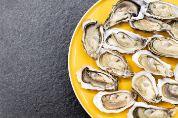 Fresh oysters ready to be eaten raw. Oysters on a yellow plate and a black stone. Raw fish with oysters, luxurious dinner and quality fresh shellfish.  Restaurant special dish