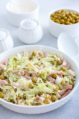 vegetable salad with cabbage, sausages and canned peas on a white plate, selective focus