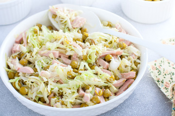 vegetable salad with cabbage, sausages and canned peas on a white plate, selective focus