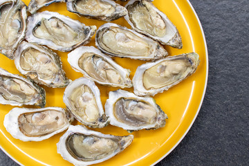 Fresh oysters ready to be eaten raw. Oysters on a yellow plate and a black stone. Raw fish with oysters, luxurious dinner and quality fresh shellfish.  Restaurant special dish