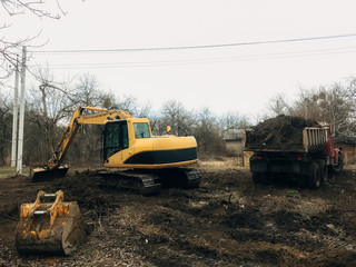 Excavator uprooting trees on land in countryside. Bulldozer clearing land from old trees, roots and branches with dirt and trash. Backhoe machinery. Yard work © sonyachny