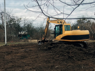 Obraz na płótnie Canvas Excavator uprooting trees on land in countryside. Bulldozer clearing land from old trees, roots and branches with dirt and trash. Backhoe machinery. Yard work