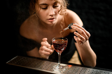 Young woman at bar adds ingredients to cocktail and looks at it