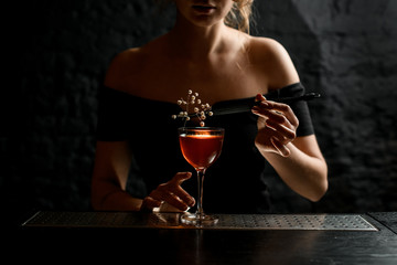 female bartender holds tweezers with white flowering branch over glass