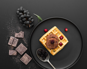 Black plate with waffles on a dark background with chocolate and grapes
