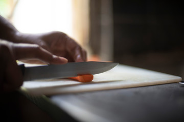 Woman cutting carrot with a knife on a chopping board in an Indian kitchen