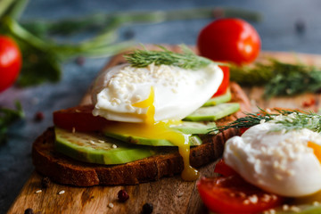 Toast with poached eggs, tomatoes, avocado, spices and herbs. Tasty breakfast on the table