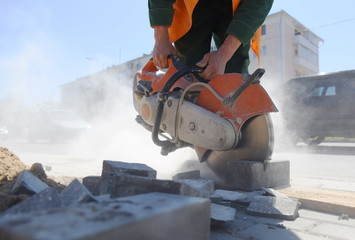 The builder saws the curb, there are a lot of concrete tiles around.