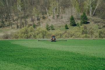 The tractor is working on a green spring field. Agriculture with cereal crops