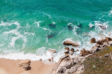 Aerial view of the sandy beach and rocky coast with the big turquoise waves of the Atlantic Ocean. Nazare, Portugal.