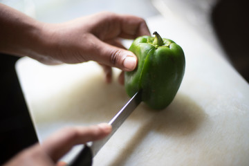Woman cutting whole green capsicum with a knife on a chopping board in an Indian kitchen