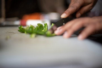 Woman chopping green capsicum with a knife on a chopping board in an Indian kitchen