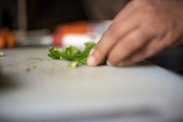 Woman chopping green capsicum with a knife on a chopping board in an Indian kitchen