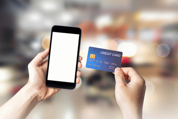 Hands holding credit card with Smart mobile phone show white screen background for your design online shopping on shopping mall background, E-payment technology, Concept of internet banking.copy space