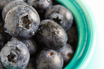 Blueberries in a turquoise pot on a light gray table close-up. Berries on the left side of the image