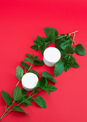 two white containers of cream with green branches on a red background
