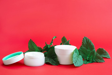 two white containers of cream with green branches on a red background
