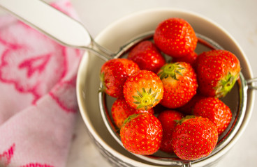 Washed strawberries and left to dry in a colander over a bowl on a light gray background, next to a kitchen towel