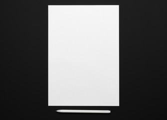 a blank sheet of paper and a pen on a black table, top view - template for any text or inscription